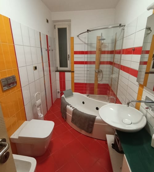 Modern bathroom with red and white tiles, bathtub with shower, sink, and toilet in Casa Bertila apartment, Ancona