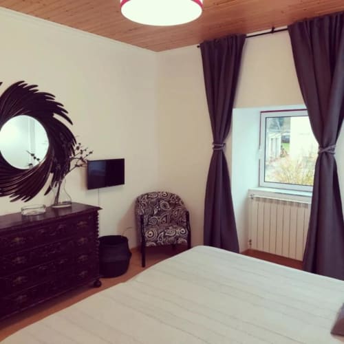 Suíte de quarto moderno na SOTAM Country House em Góis com móveis de madeira escura, cortinas roxas e janela com vista para o jardim