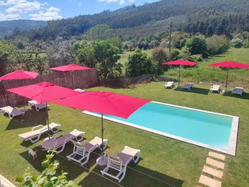 Piscina azul-turquesa com guarda-sóis e espreguiçadeiras cor-de-rosa na SOTAM Country House, retiro rural português perto de Góis