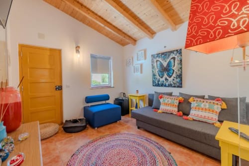 Suite colorida na SOTAM Country House com sofá cinzento, puf azul, vigas de madeira e vista para o jardim em Góis