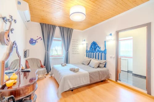 Quarto luminoso da SOTAM Country House com teto de madeira, cabeceira azul, decoração com violão e vista para o jardim