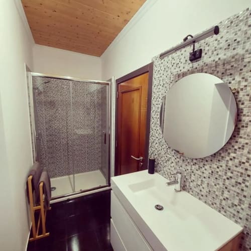 Banheiro moderno na SOTAM Country House com pia branca, espelho redondo, revestimento de azulejo mosaico e box de vidro
