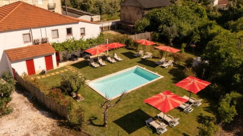 Área da piscina da Country House SOTAM com guarda-sóis vermelhos, espreguiçadeiras e jardim em Góis, Portugal