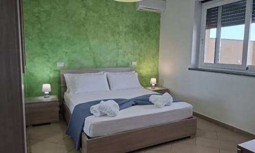 Camera moderna con parete accent verde, biancheria bianca e finestra con vista mare all'hotel Gold Leaf Sicily di Taormina