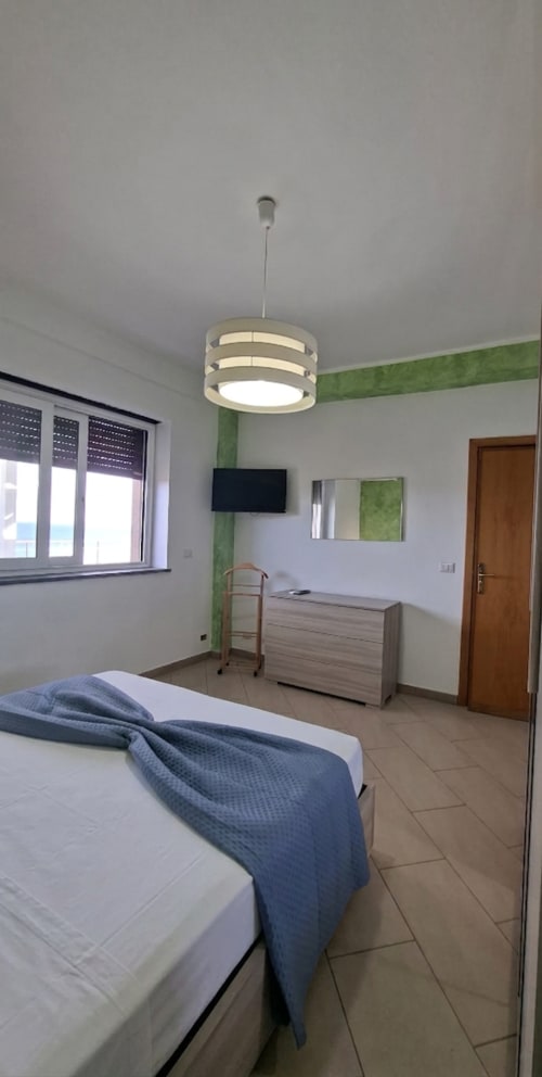 Camera da letto moderna con vista mare nell'appartamento Cleopatra di Gold Leaf Sicily, con biancheria blu, lampada a sospensione e dettagli verdi