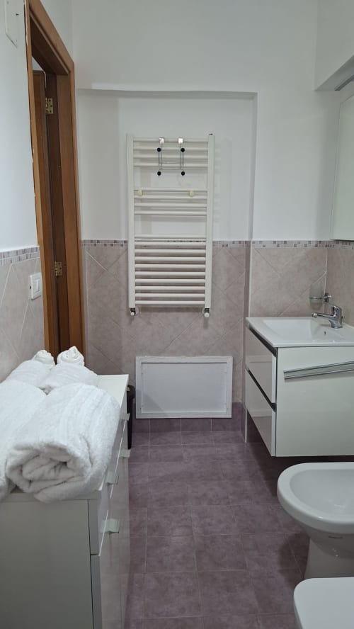 Bagno moderno a Gold Leaf Sicily con scaldasalviette, lavabo bianco, toilette e pavimento piastrellato nell'appartamento di Taormina