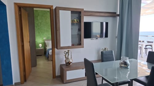 Soggiorno dell'appartamento Cleopatra con vista mare, TV a schermo piatto, arredi in legno e accesso al balcone a Taormina, Sicilia