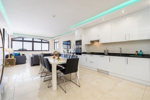 Modern open-plan kitchen and dining area in Marbella beachfront apartment with white cabinetry, black counters, and dining