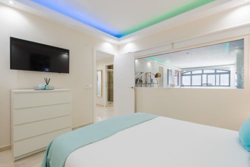Modern bedroom in Marbella beachfront apartment with white bed, flat-screen TV, dresser, and turquoise accents