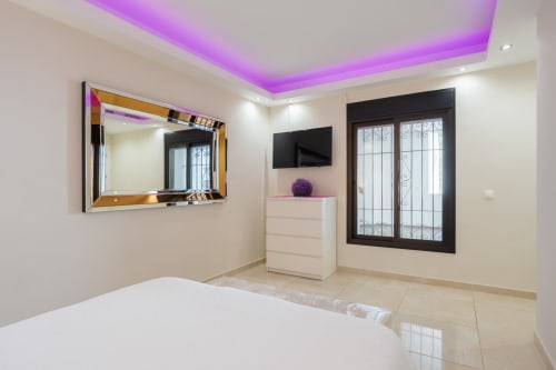 Modern beachfront apartment bedroom in Puerto Banús, Marbella with purple ceiling lights, flat-screen TV, and elegant