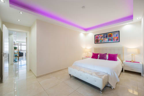 Modern beachfront apartment bedroom in Marbella with purple ceiling lighting, white bed, and pop art decor