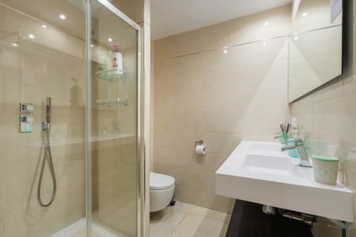 Modern bathroom in Marbella beachfront apartment with glass shower enclosure, white sink, and neutral tile finishes