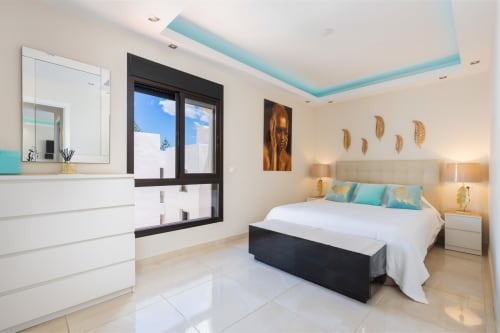 Modern Marbella beachfront apartment bedroom with turquoise ceiling details, white bedding, and en-suite bathroom.