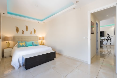 Modern bedroom in Marbella beachfront apartment with turquoise ceiling, queen bed, gold accents, and ensuite bathroom