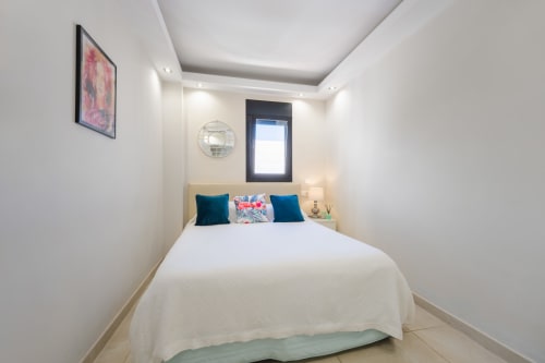 Modern bedroom in Marbella beachfront apartment with white bedding, teal pillows, and contemporary lighting