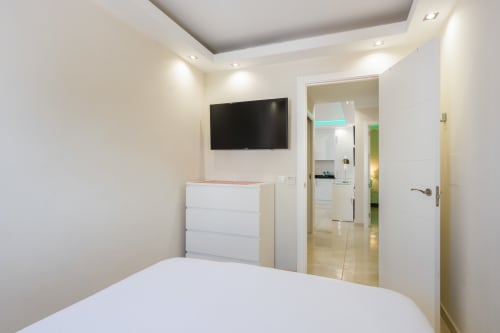 Modern bedroom with flat-screen TV, white dresser, and open bathroom at Marbella Home Rentals beachfront apartment