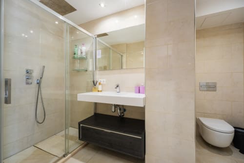 Modern bathroom with beige tile, glass shower enclosure, white sink, and black vanity in Marbella beachfront apartment