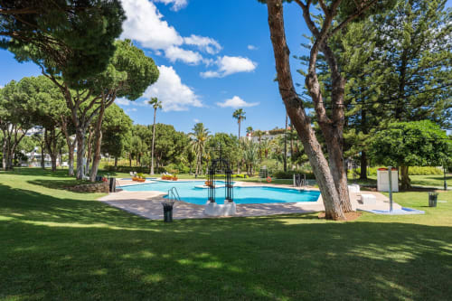 Luxurious pool area surrounded by mature trees and manicured lawn at Marbella Home Rentals, Puerto Banús beachfront apartment