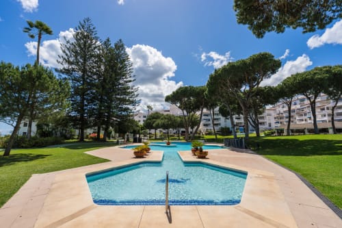 Luxury beachfront apartment pool area in Marbella with lounge chairs, lush gardens and modern apartment buildings.
