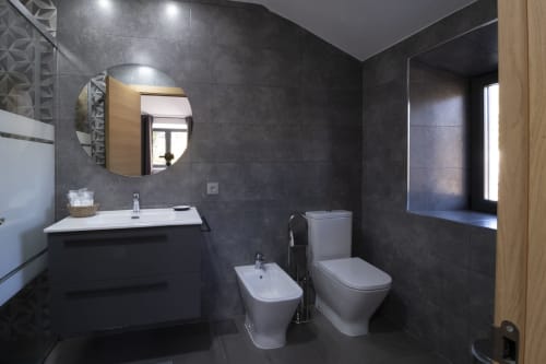 Baño moderno con azulejos oscuros, accesorios blancos, espejo redondo y puerta de madera del Hotel Spa El Batán