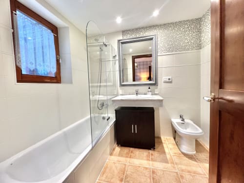 Baño moderno con azulejos blancos, ducha de cristal, tocador oscuro y espejo en el apartamento Eth Narjò en Vielha