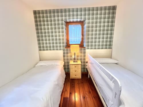Habitación twin en el apartamento Eth Narjò, Vielha, con suelo de madera, ropa de cama blanca, papel pintado de cuadros y vistas a la montaña