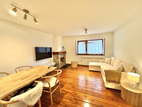 Amplio salón con suelos de madera, chimenea, televisor, mesa de comedor y sofá crema en el apartamento de Vielha