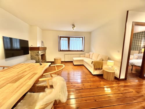 Salón moderno en Vielha con suelos de madera, sofá crema, chimenea y vistas a la montaña