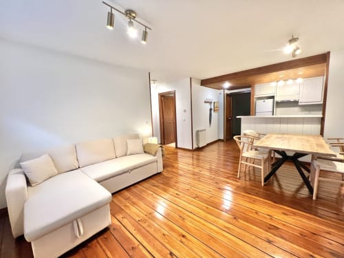 Apartamento moderno diáfano en Vielha con sofá crema, mesa de comedor, suelo de madera y cocina equipada con Nespresso