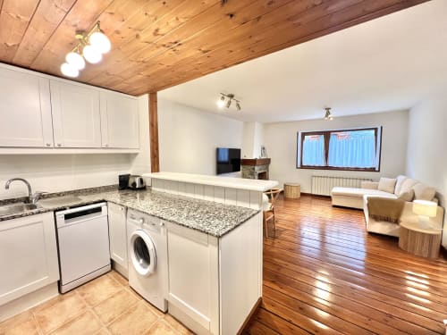 Cocina y sala de estar modernas en Vielha con encimeras de granito, armarios blancos, techo de madera y suelo de madera