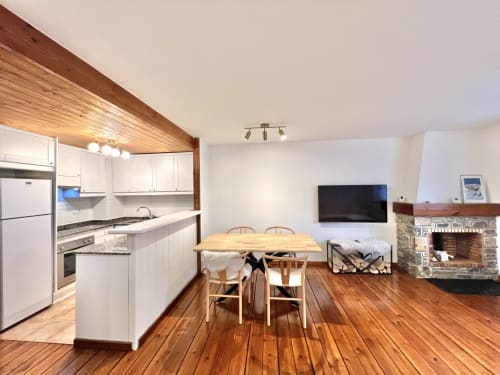 Cocina y sala de estar modernas en Vielha con suelos de madera, gabinetes blancos, mesa de comedor, chimenea y televisión