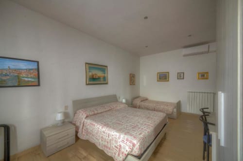 Camera quadrupla presso Sogni D'Oro Guest House a Firenze con letti matrimoniali e singoli, pavimento in legno e quadri incorniciati su pareti bianche