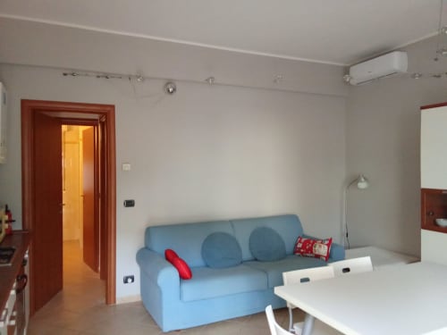 Moderno soggiorno in appartamento a Rho con divano blu, tavolo da pranzo bianco, porta rossa e dotazioni cucina