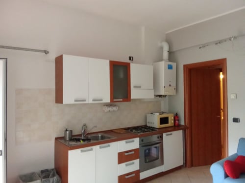 Cucina moderna con mobili bianchi e rossi, fornello, forno e lavello nell'appartamento My Home Rapallo, Rho