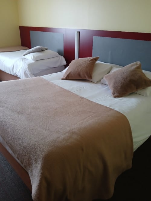 Chambre triple à Libre Hôtel avec lits jumeaux, literie beige et marron, tête de lit moderne rouge et gris, vue sur jardin