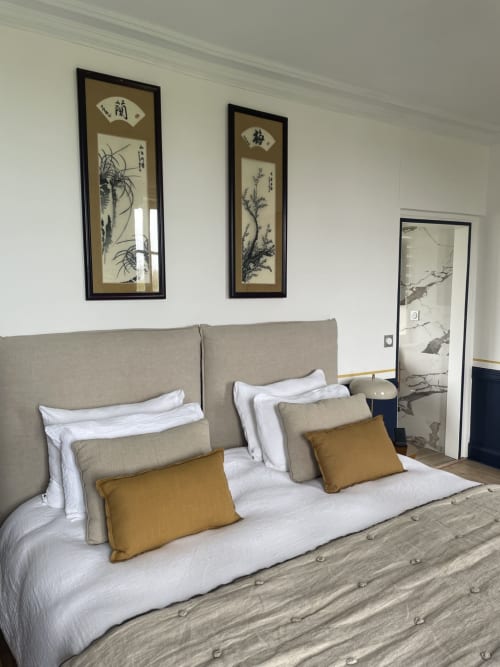 Chambre moderne au domaine de Marculfo avec lit capitonné beige, literie blanche, oreillers ocre et œuvres d'art asiatiques