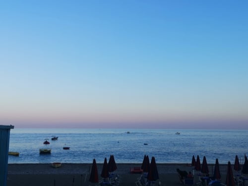 La spiaggia serena di Taormina al tramonto con barche ormeggiate, ombrelloni e le tranquille acque del Mediterraneo a Gold Leaf Sicily