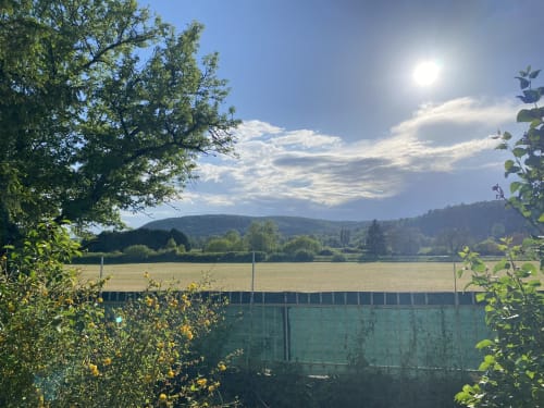 Vue pittoresque du jardin des Gîtes de l'Impériale à Sermizelles avec champs verts, collines boisées et ciel bleu