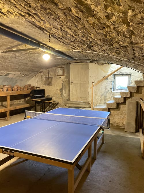 Salle de loisirs souterraine aux Gîtes de l'Impériale avec tables de ping-pong, étagères en bois et plafond voûté en pierre