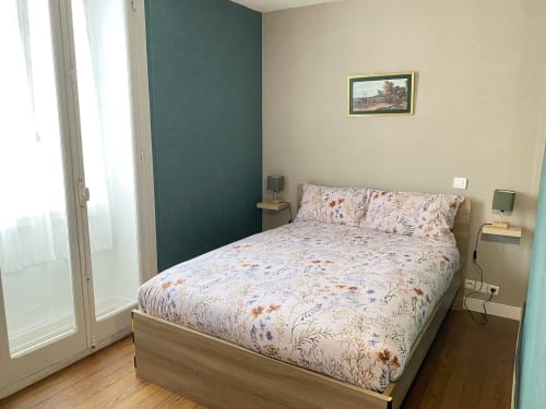 Chambre douillette aux Gîtes de l'Impériale à Sermizelles avec literie fleurie, mur accent bleu-vert, vue jardin et design moderne