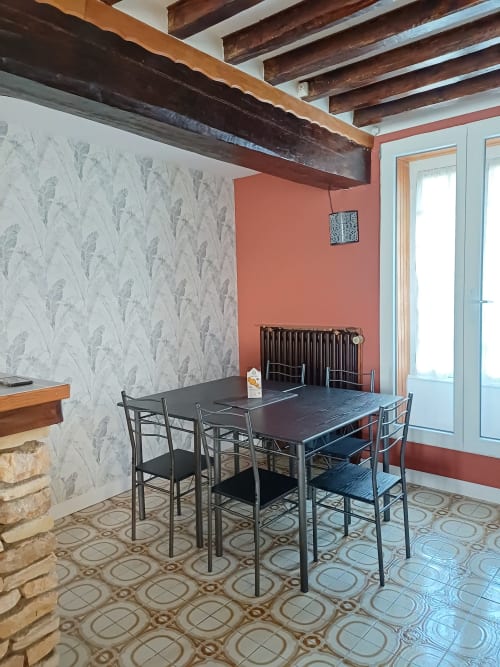 Salle à manger des Gîtes de l'Impériale à Sermizelles avec table noire, chaises, poutres apparentes et mur accent corail