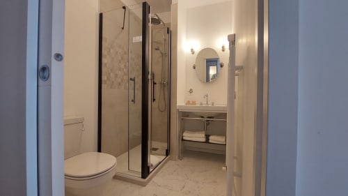 Bagno moderno dell'Hotel Dandy Rouen con cabina doccia in vetro, lavabo, specchio rotondo e pavimento in marmo