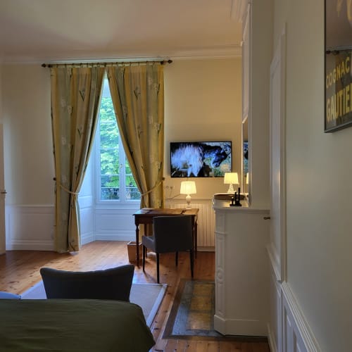 Élégante chambre Bassac aux Logis des Tourelles à Cognac avec vue sur jardin, bureau, TV et rideaux jaunes