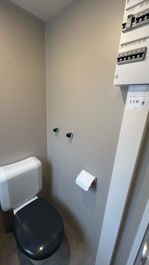 Salle d'eau compacte du Mobil Home Magnolia à Camping La Lézardière avec sanitaires blancs et panneau électrique mural