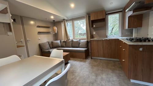Intérieur moderne de mobil-home à Camping La Lézardière avec cuisine, salle à manger, canapé-lit et vue sur le jardin