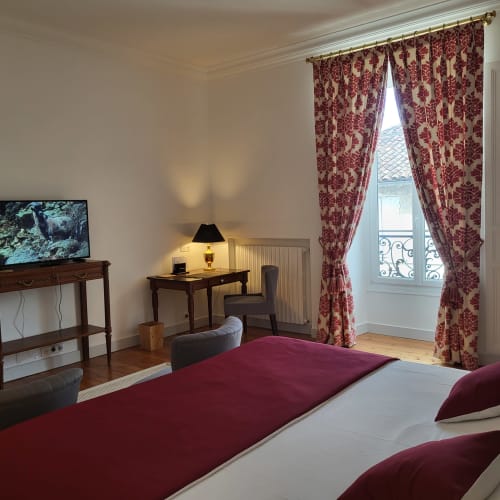 Chambre élégante du Logis des Tourelles à Cognac avec literie bordeaux, rideaux ornés, bureau et vue sur la ville