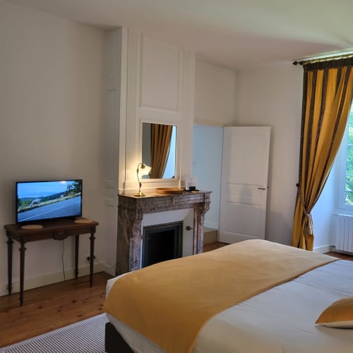 Chambre élégante des Logis des Tourelles à Cognac avec vue sur le jardin, cheminée, TV et rideaux dorés