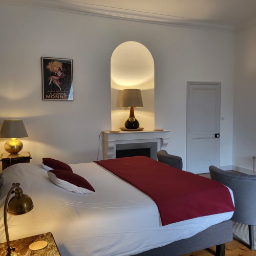 Chambre élégante au Logis des Tourelles à Cognac avec lit blanc, linge de lit bordeaux et foyer avec lampe