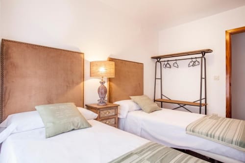 Dormitorio rústico con dos camas, cabeceros tapizados en beige y estructura de dosel de hierro en el hotel Rustikalpuente, España