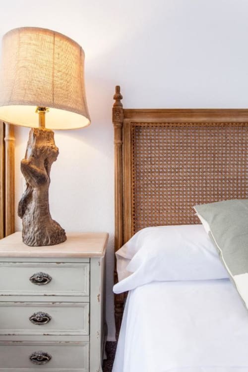 Lámpara de mesa de noche rústica con base de madera junto a cama con cabecero de ratán tejido en hotel Rustikalpuente